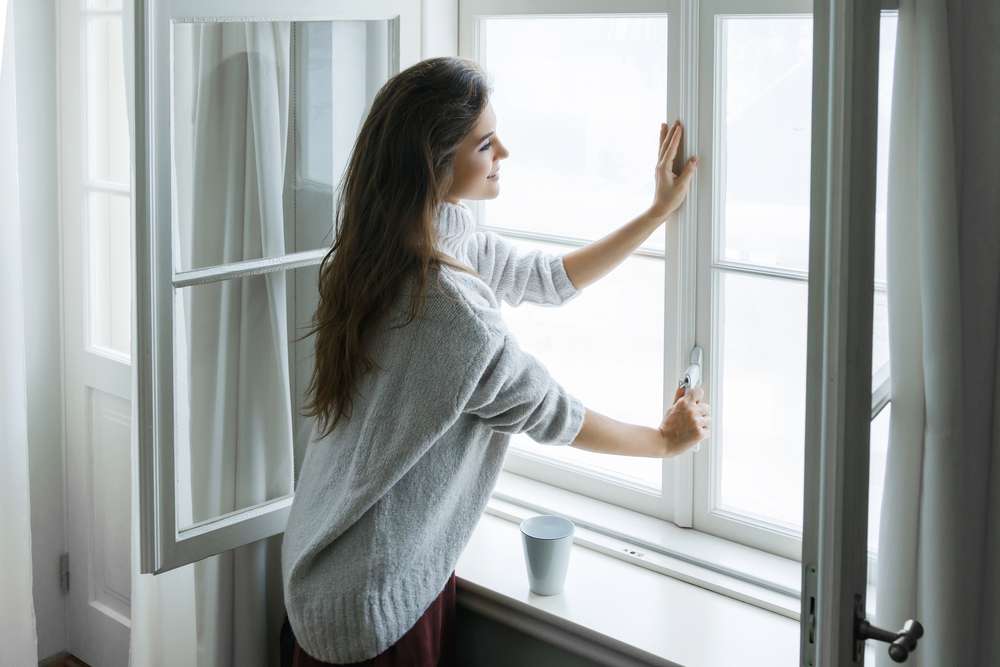 A woman unlocks her bedroom window with one pane already open.